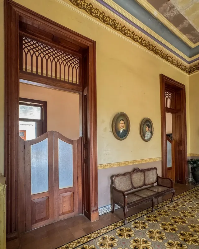 Corredor con dos retratos ovalados, una banca antigua y puertas de madera con celosía