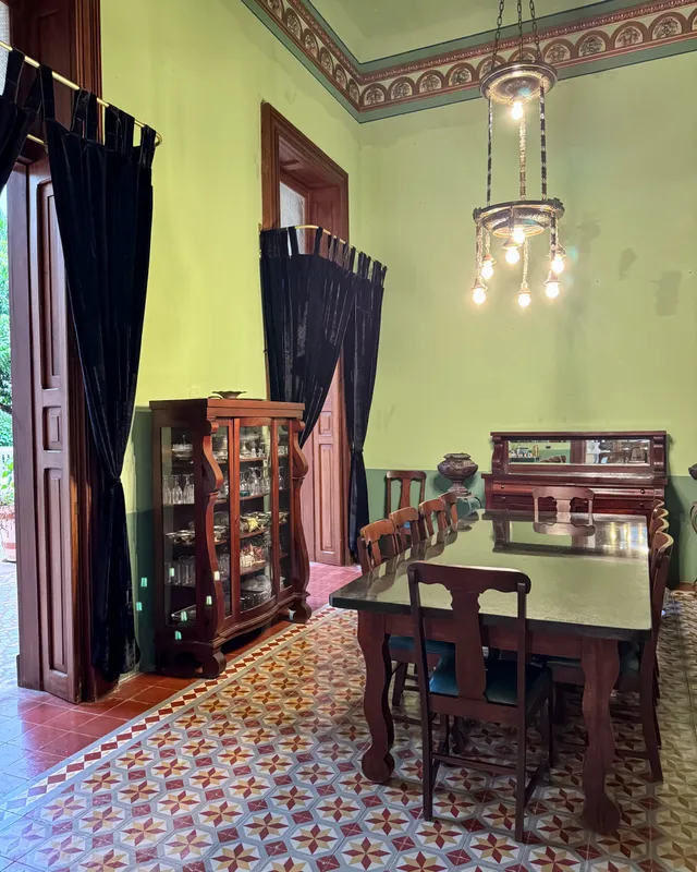 Comedor de paredes verdes con mesa larga de madera, vitrina y candil