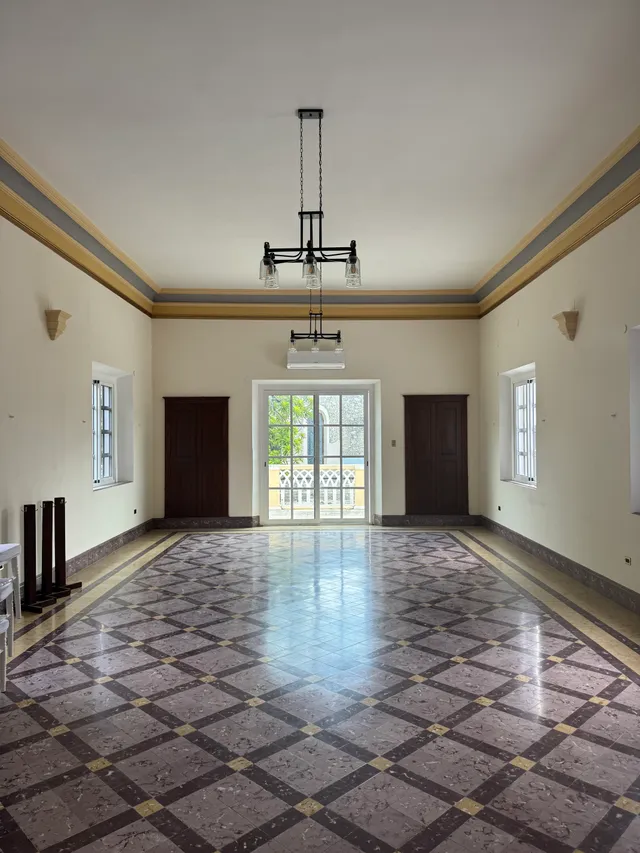 Salón amplio y vacío con piso de mármol a cuadros, candil central y puertas al balcón