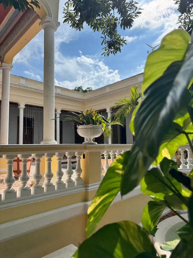 Barandal del área central con una urna blanca con plantas, entre columnas y follaje