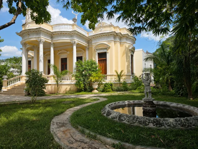 Fachada amarilla de Casona Cicero vista desde el jardín, con la fuente y su estatua en primer plano