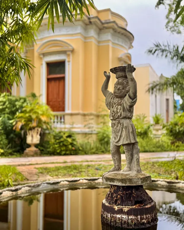 Estatua de niño sobre una fuente, con la fachada amarilla de fondo