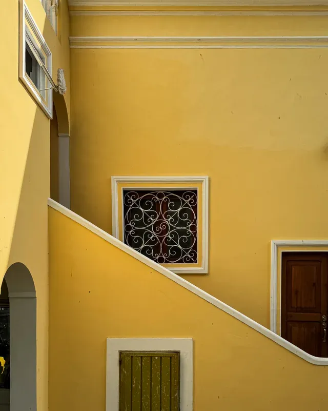 Detalle de la fachada amarilla con escalera exterior y ventana con reja decorativa