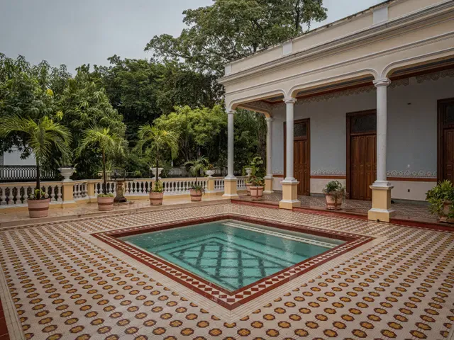 Alberca y corredor restaurados de Casona Cicero, con columnas y macetas junto al jardín